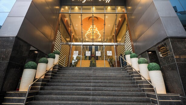 Een hotelentree met een trap die leidt naar een receptie, uitgevoerd in een modern design met een glazen gevel en een opvallend bord met de tekst 