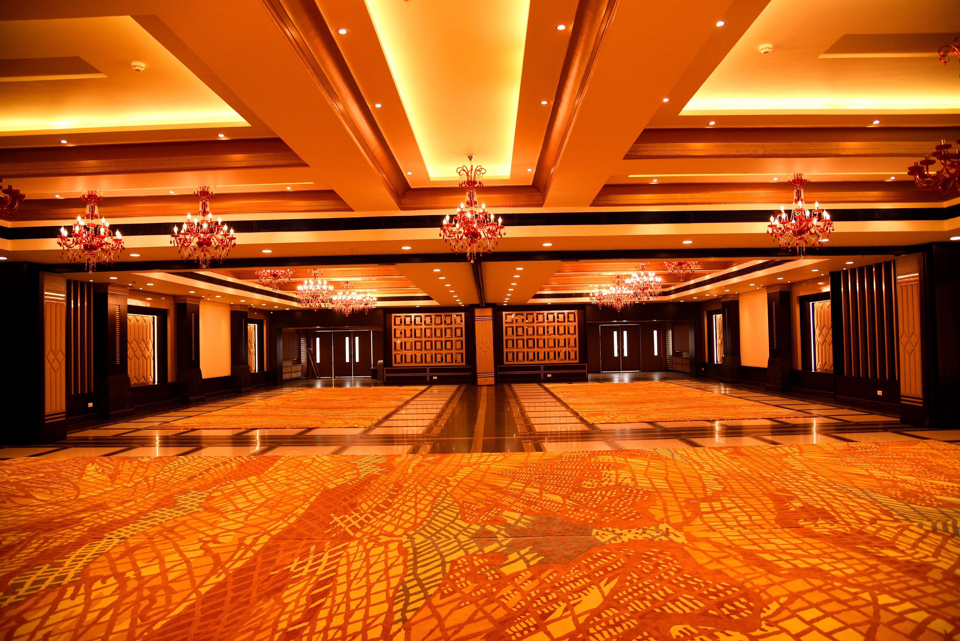 A spacious hotel lobby with a patterned carpet, chandeliers, and a symmetrical design.
