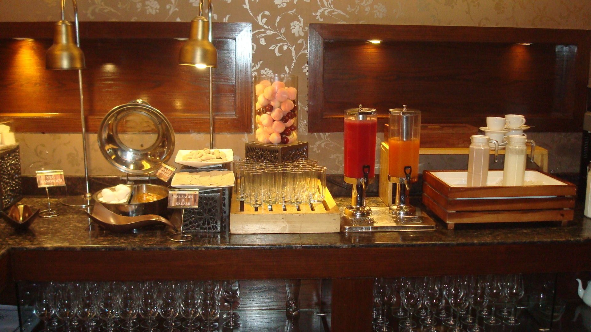 Un mostrador de buffet con diversas opciones de comida, incluyendo salchichas y salami, y una selección de bebidas.