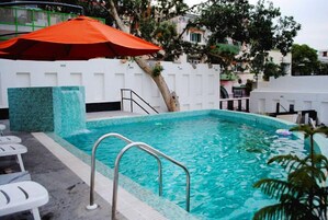 A swimming pool with a metal ladder, a red umbrella, and white lounge chairs.