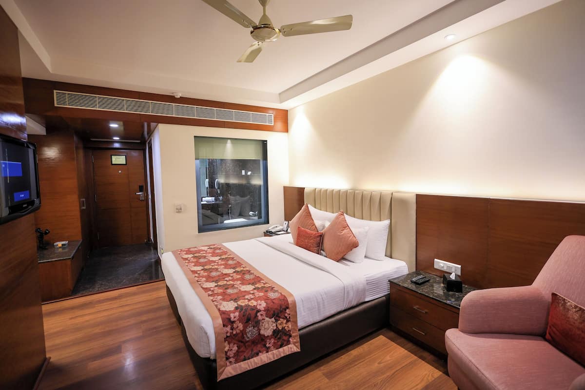 A hotel room with a bed, a TV, a ceiling fan, a window, and a wooden floor.