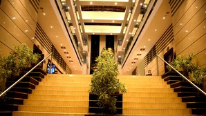 Een statige trap in een modern gebouw met meerdere verdiepingen, omzoomd door potplanten en verlicht door plafondlampen.