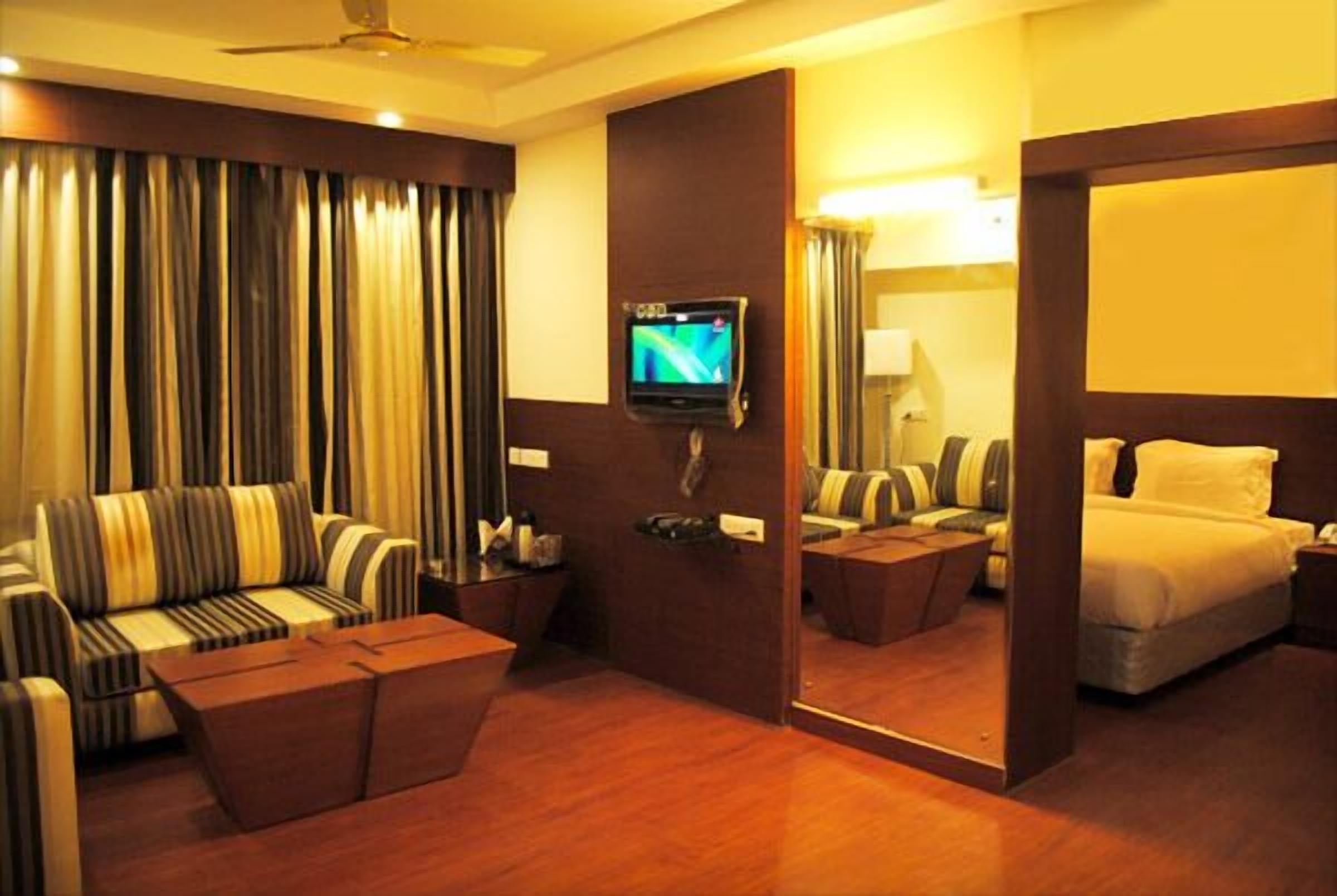 A hotel room with a sofa, a bed, a TV, and a mirror.