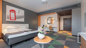 A hotel room with a bed, a small round table with a vase of flowers, a desk with a chair, and a mirror.