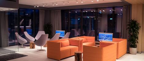 A modern lobby with orange sofas, a glass wall, and a large screen displaying a cityscape.