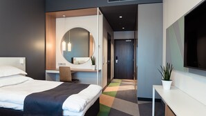 Una habitación de hotel moderna con una cama grande, un escritorio, un espejo redondo y un televisor.