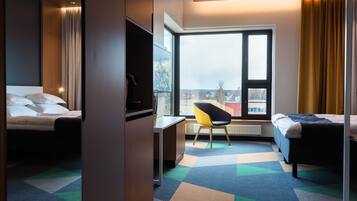 A hotel room with two beds, a desk, a chair, and a large window with a view of buildings.