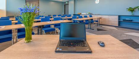 A classroom with a laptop on a desk, blue chairs, and a vase of flowers.