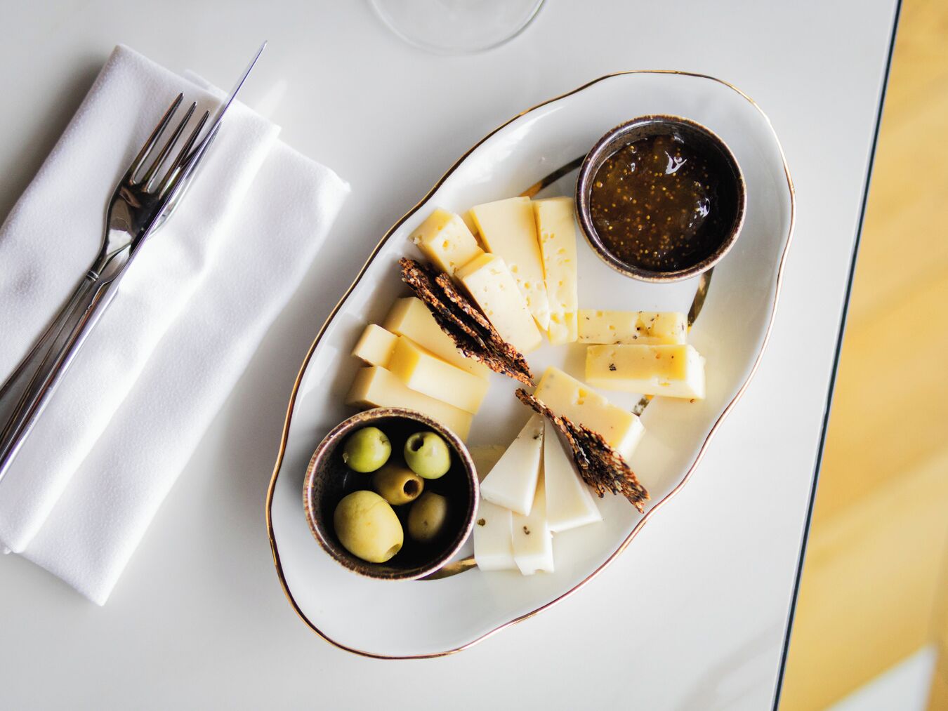 Un plato con queso, aceitunas y salsa para mojar sobre una mesa blanca.