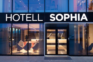 Una entrada de hotel moderna con fachada de vidrio, mostrador de recepción y zonas de estar contemporáneas.