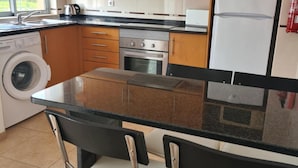 A modern kitchen with wooden cabinets, a stainless steel oven, a microwave, and a refrigerator. There is a washing machine and a sink with a faucet.