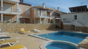 A swimming pool with lounge chairs, a stone wall, and multi-story buildings with balconies.