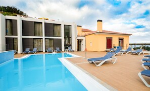 A swimming pool with lounge chairs, a building with large windows, and a red door. - Hotel Solar do Bom Jesus (Santa Cruz)