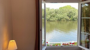 Un dormitorio con cama, ventana con cortinas, lámpara y vista a un lago.