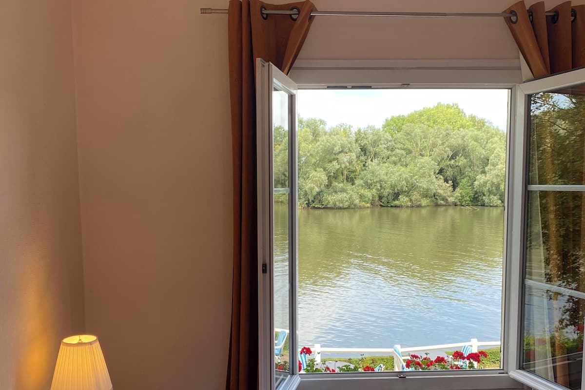 A bedroom with a bed, a window with curtains, a lamp, and a view of a lake.