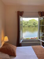 Un dormitorio con cama, ventana con cortinas, lámpara y vista a un lago.