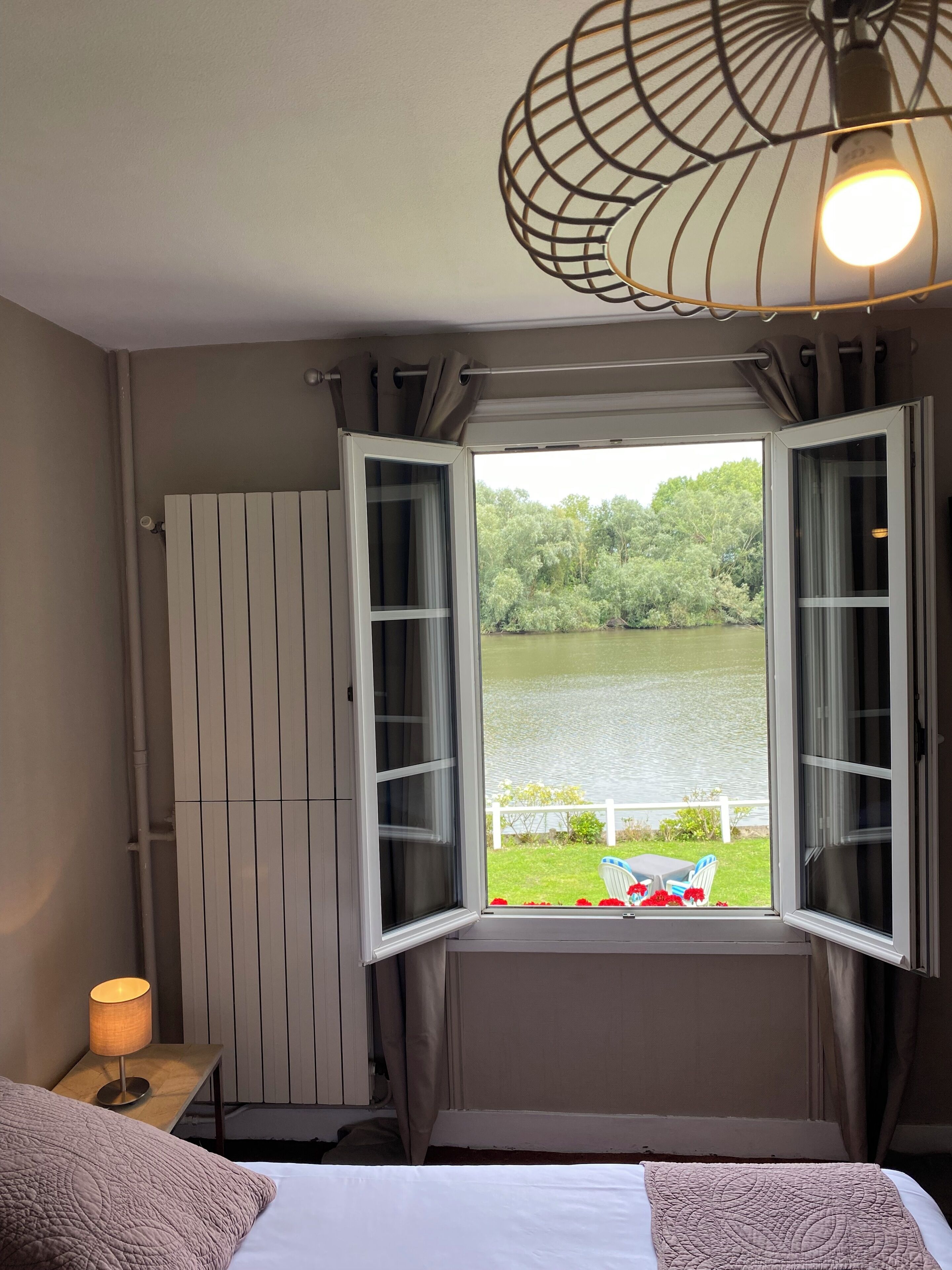 A bedroom with a bed, a bedside lamp, a window with curtains, and a view of a lake.