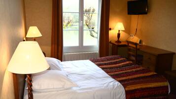 A hotel room with a bed, two bedside lamps, a TV mounted on the wall, and a window with curtains.
