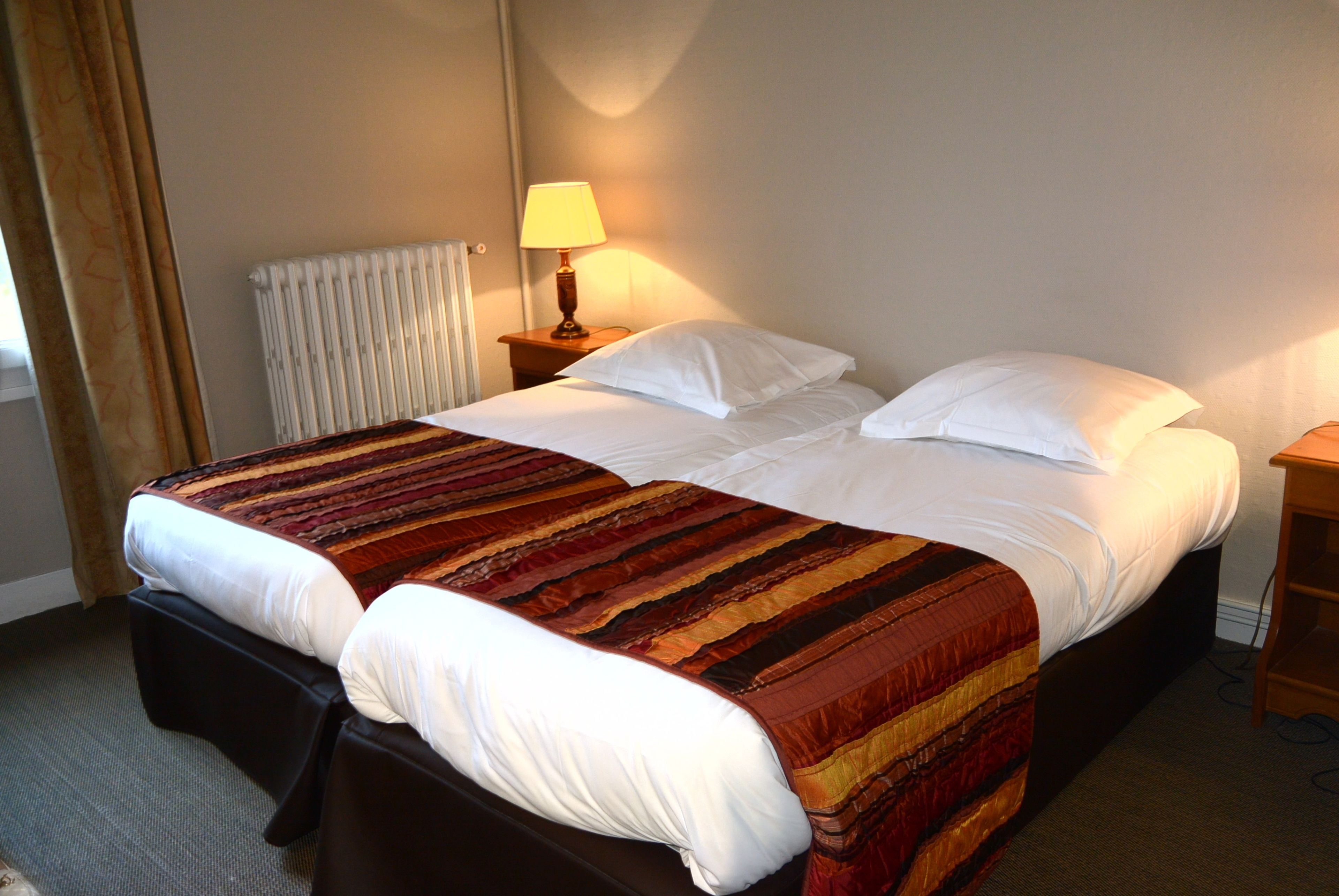 A neatly made bed with a striped blanket, a bedside lamp, and a radiator.