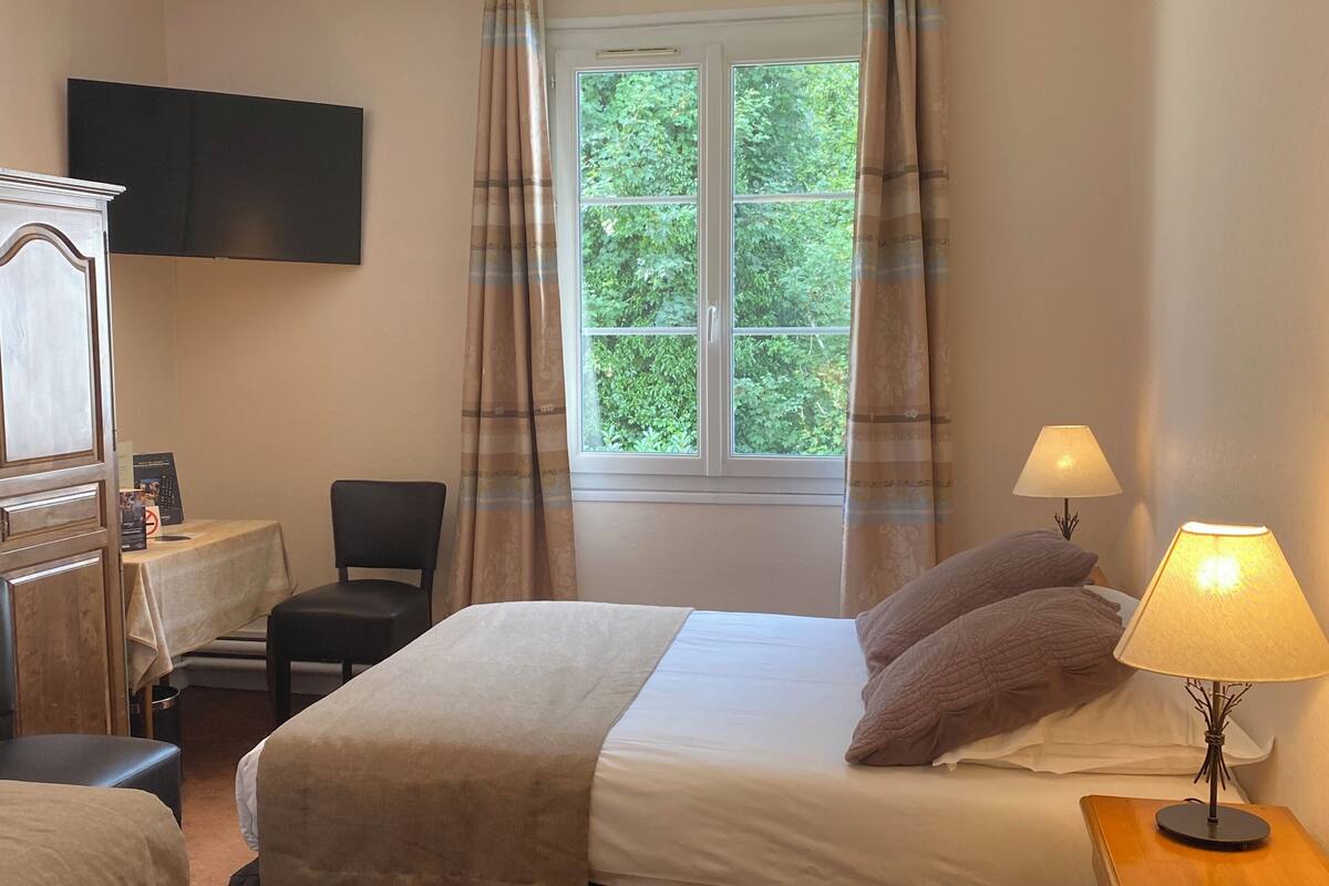A bedroom with a bed, bedside lamps, a desk, a chair, a television, and a window with curtains.