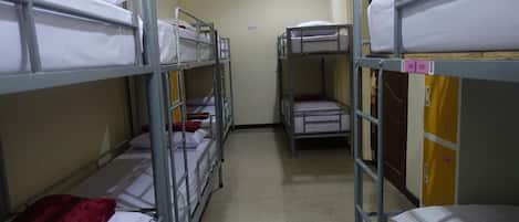 Un pasillo con literas dispuestas en dos filas, cada una con colchón y almohadas.