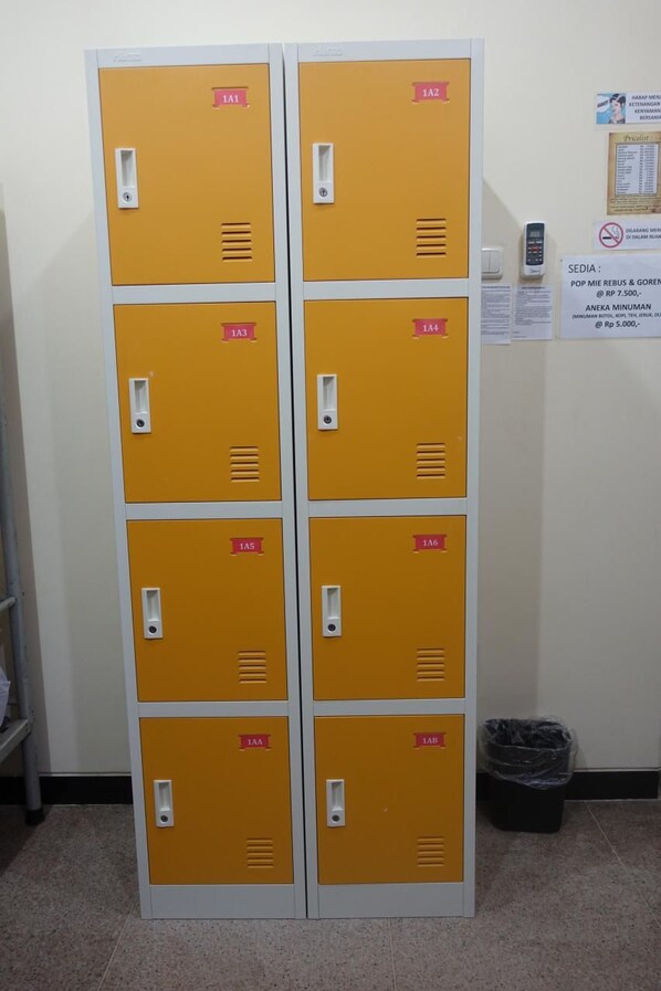 A set of yellow lockers with numbered labels, a trash bin, and a notice board with various signs.
