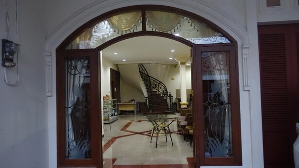 An arched doorway leading to a room with a staircase, a dining area, and a sofa. - The Backpacker Semarang - Hostel (Semarang)