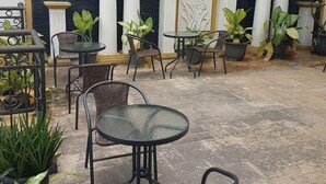 An outdoor patio area with round tables and wicker chairs, surrounded by potted plants. - The Backpacker Semarang - Hostel (Semarang)
