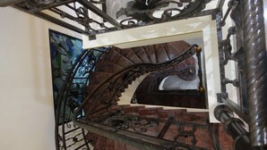 A spiral staircase with ornate metal railings and a stained glass window in the background. - The Backpacker Semarang - Hostel (Semarang)