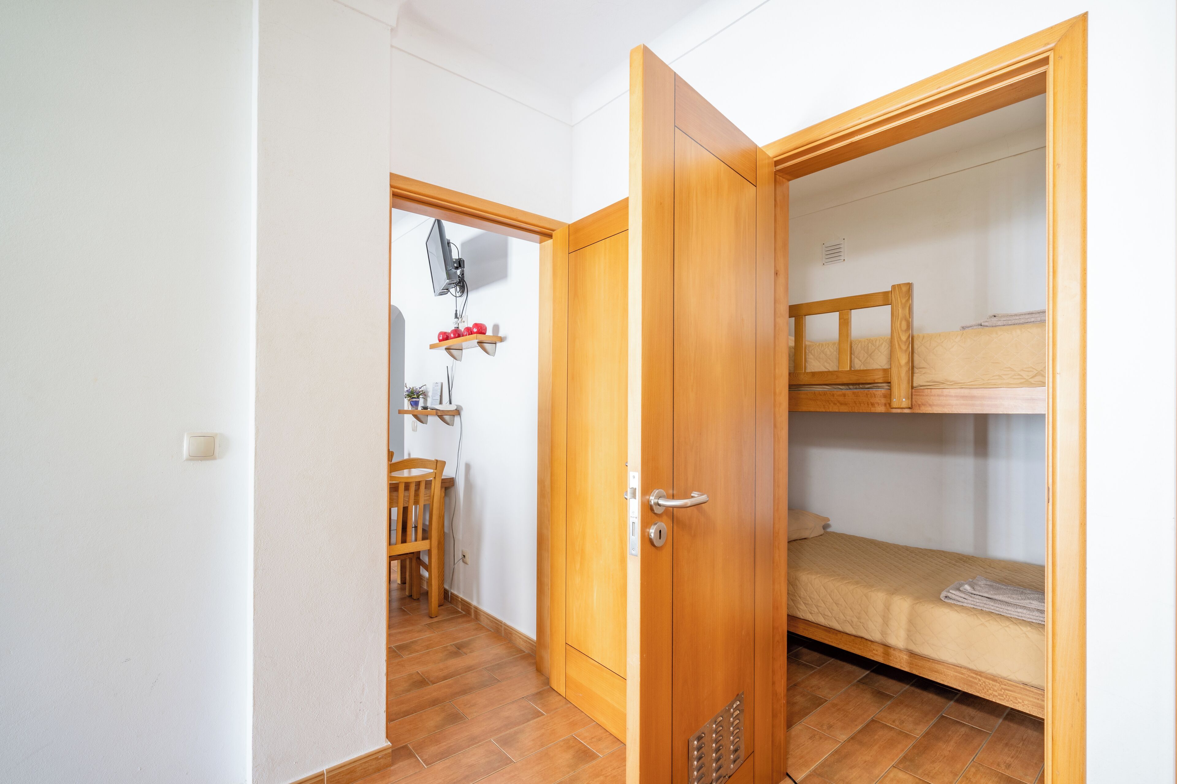 A room with a wooden door, a bunk bed, and a small table with a chair.