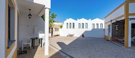 A courtyard with cobblestone flooring, white buildings, and a clear blue sky.