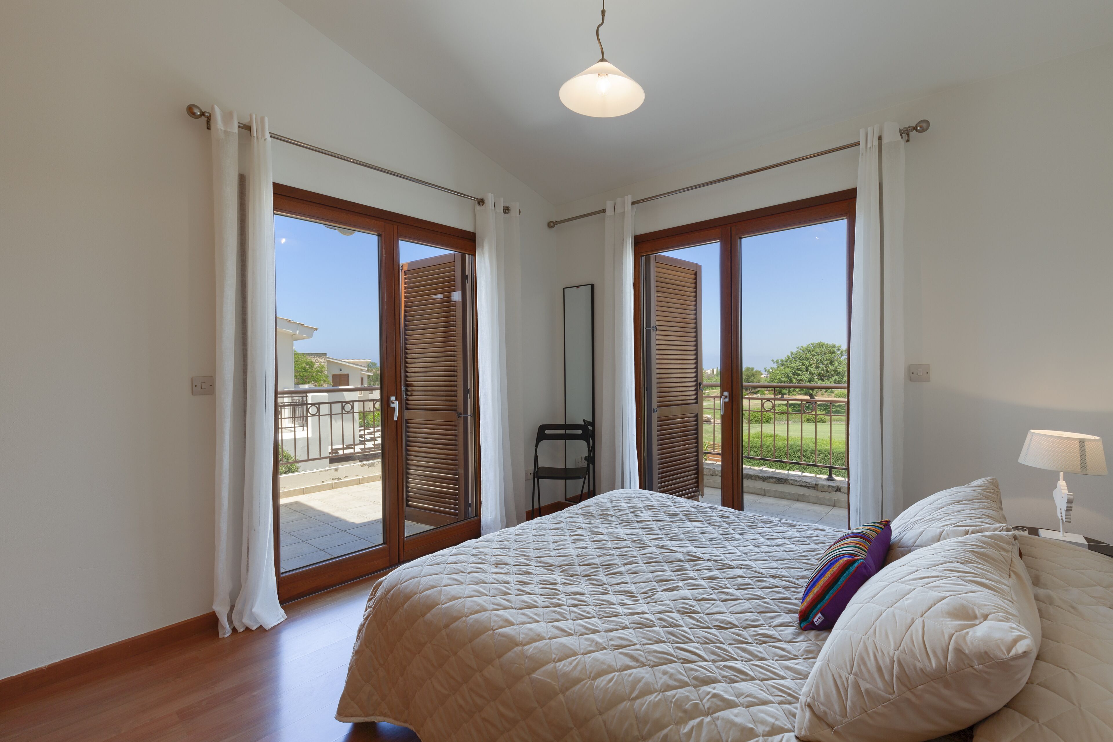 Un dormitorio con una cama grande, una mesita de noche, una lámpara y vistas al exterior por una puerta corrediza de vidrio.