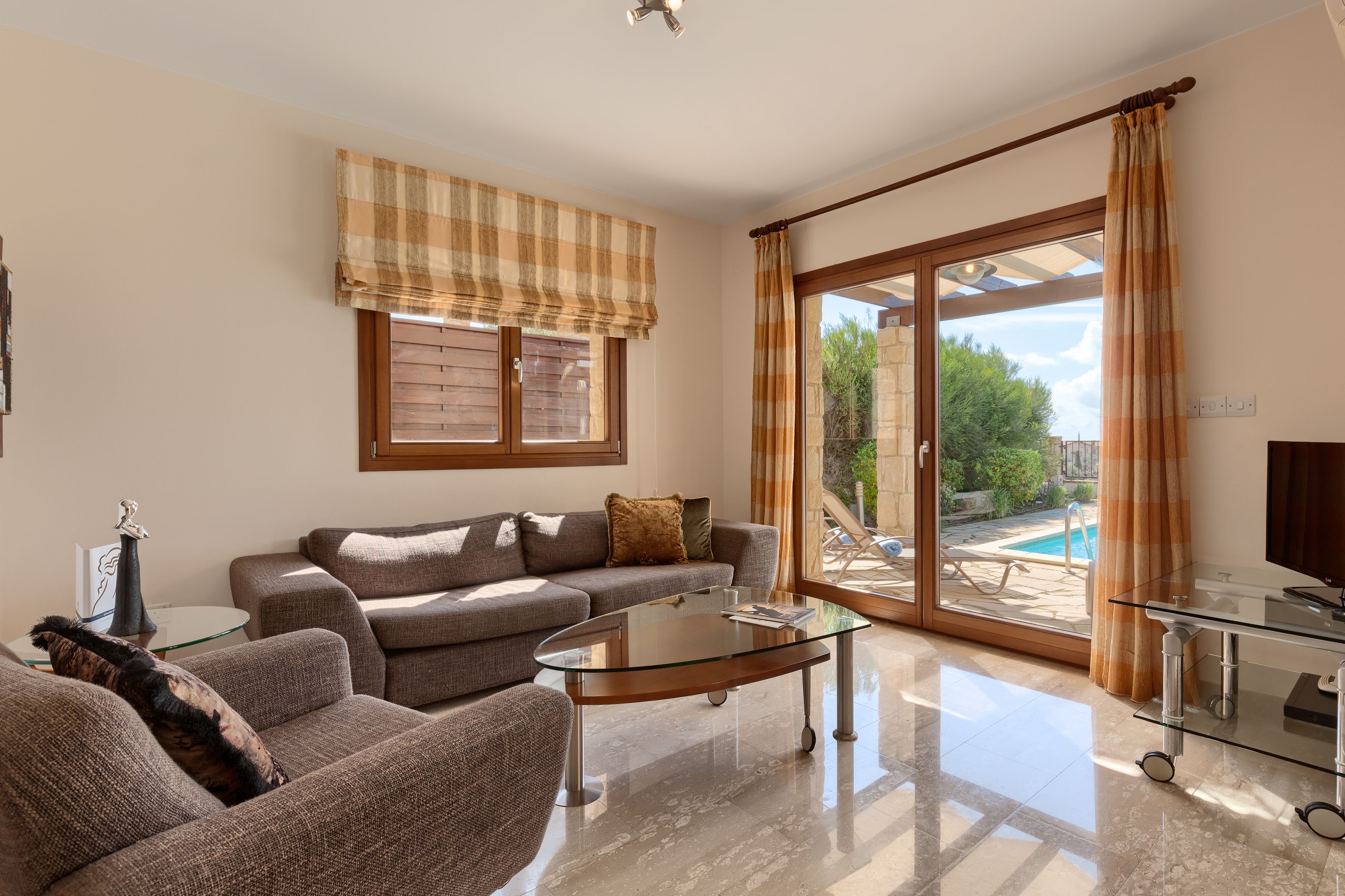 A living room with a sofa, a glass coffee table, and a TV. There is a sliding glass door leading to a pool area.