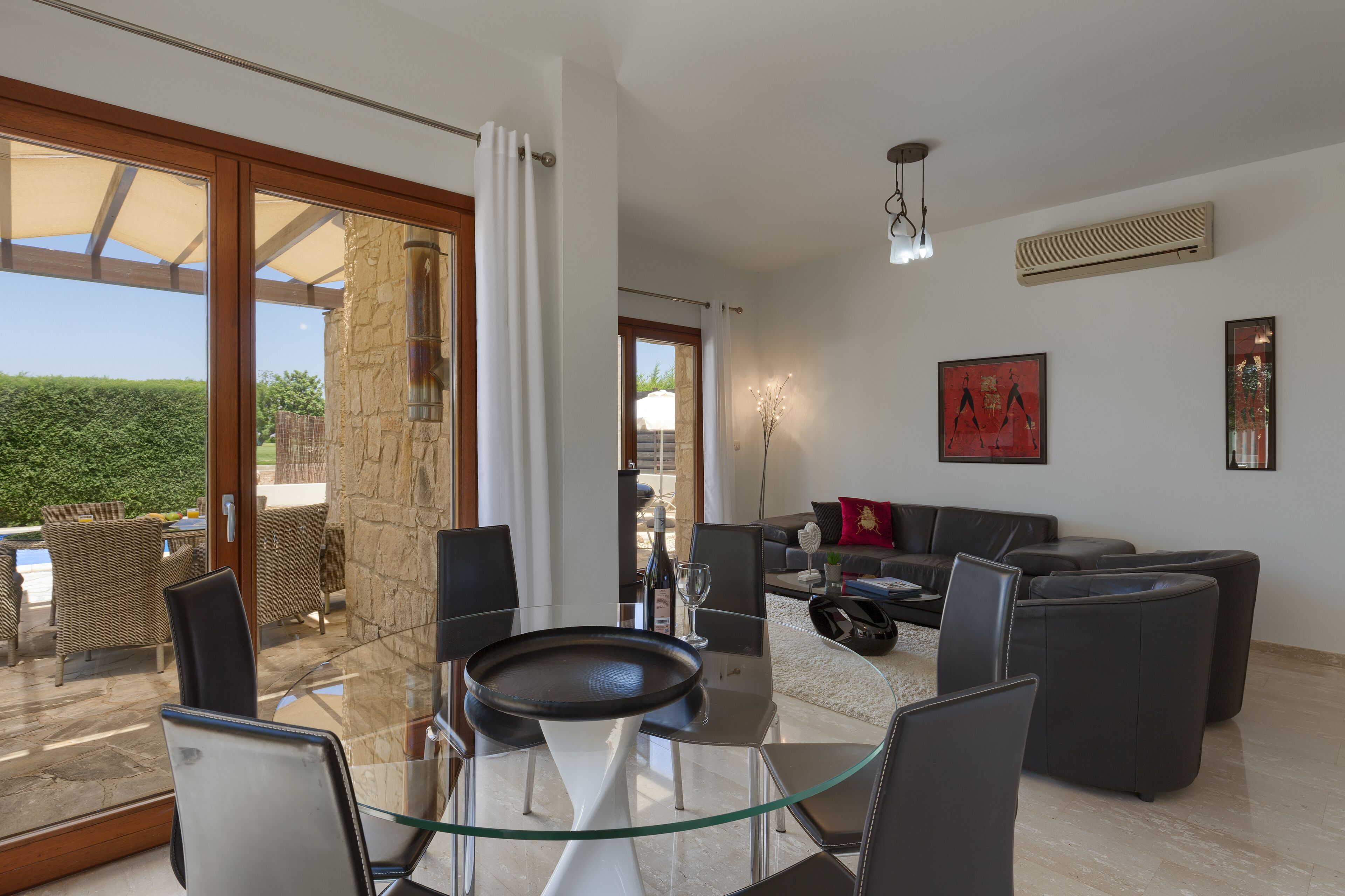 A modern living room with a glass table, dark sofas, and a view of the outdoors.