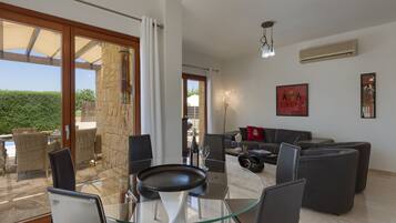 A modern living room with a glass table, dark sofas, and a view of the outdoors.