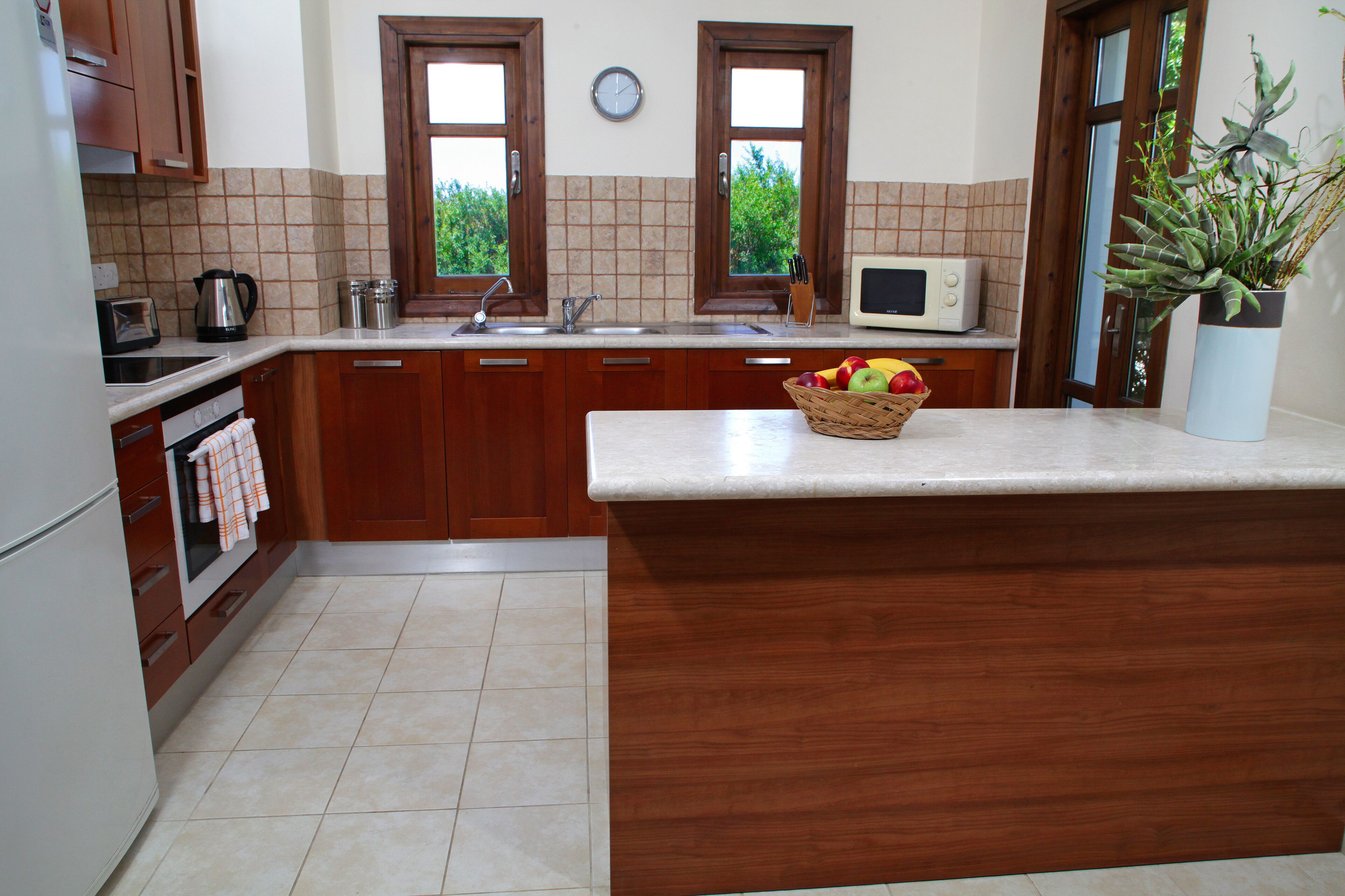 A kitchen with wooden cabinets, a microwave, a sink, and a fruit basket on the counter.