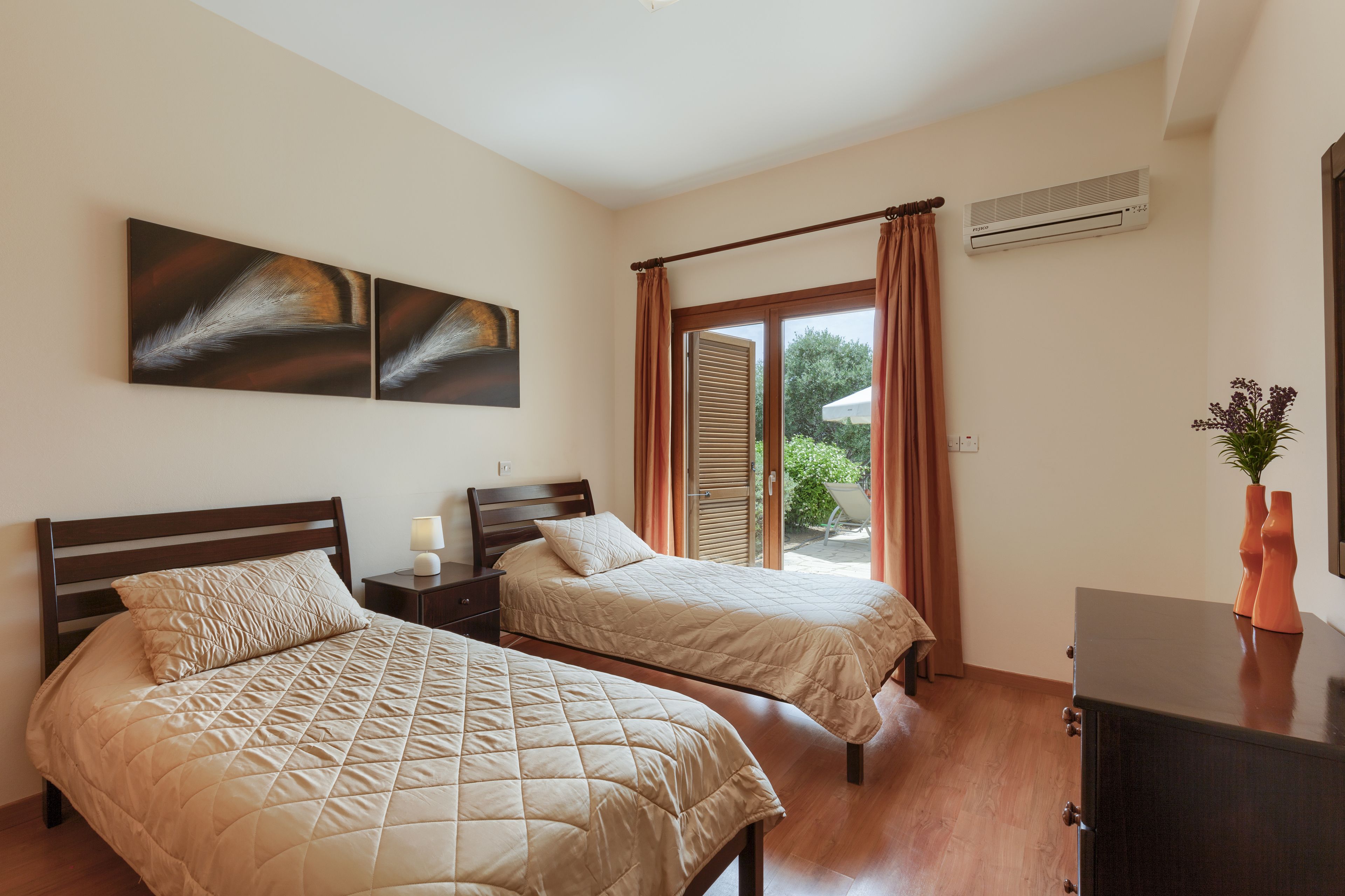 Een slaapkamer met twee bedden, een nachtkastje, een dressoir, een raam met gordijnen en kunst aan de muur.