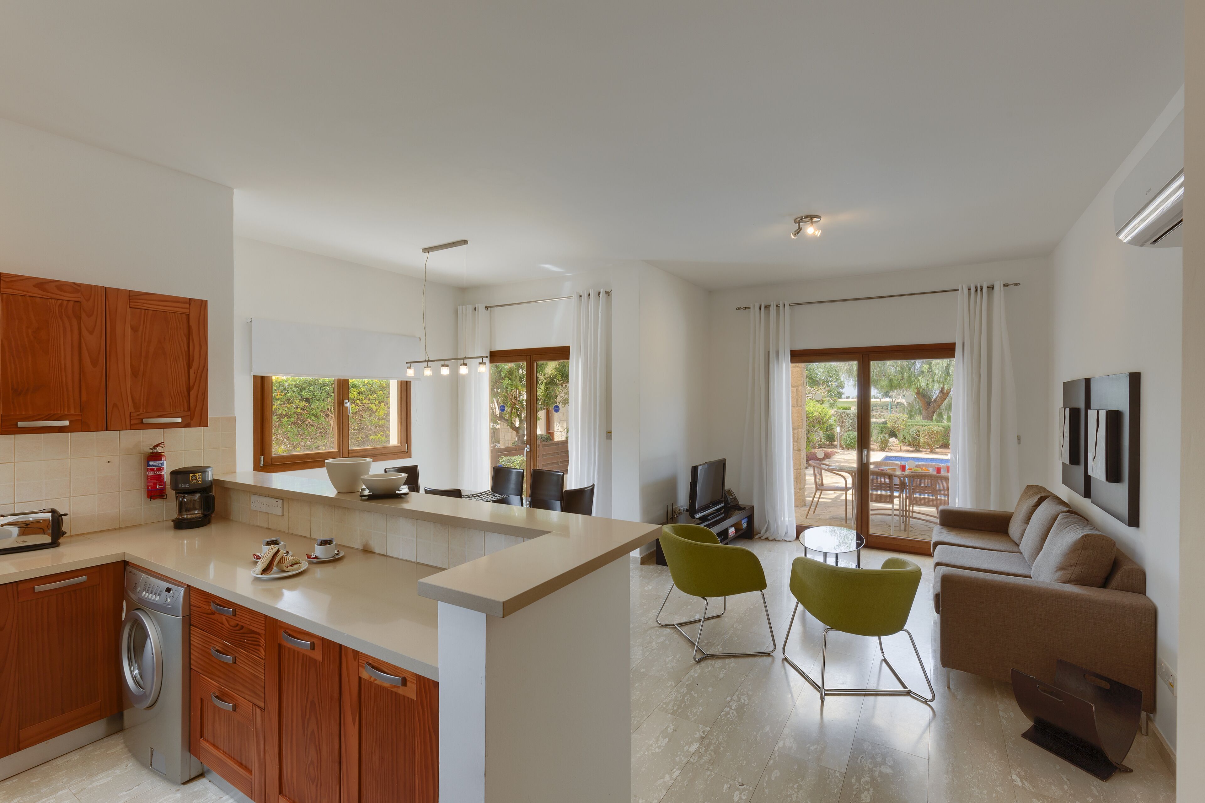 A modern kitchen with wooden cabinets, a built-in washing machine, and a dining area with a sofa and chairs.