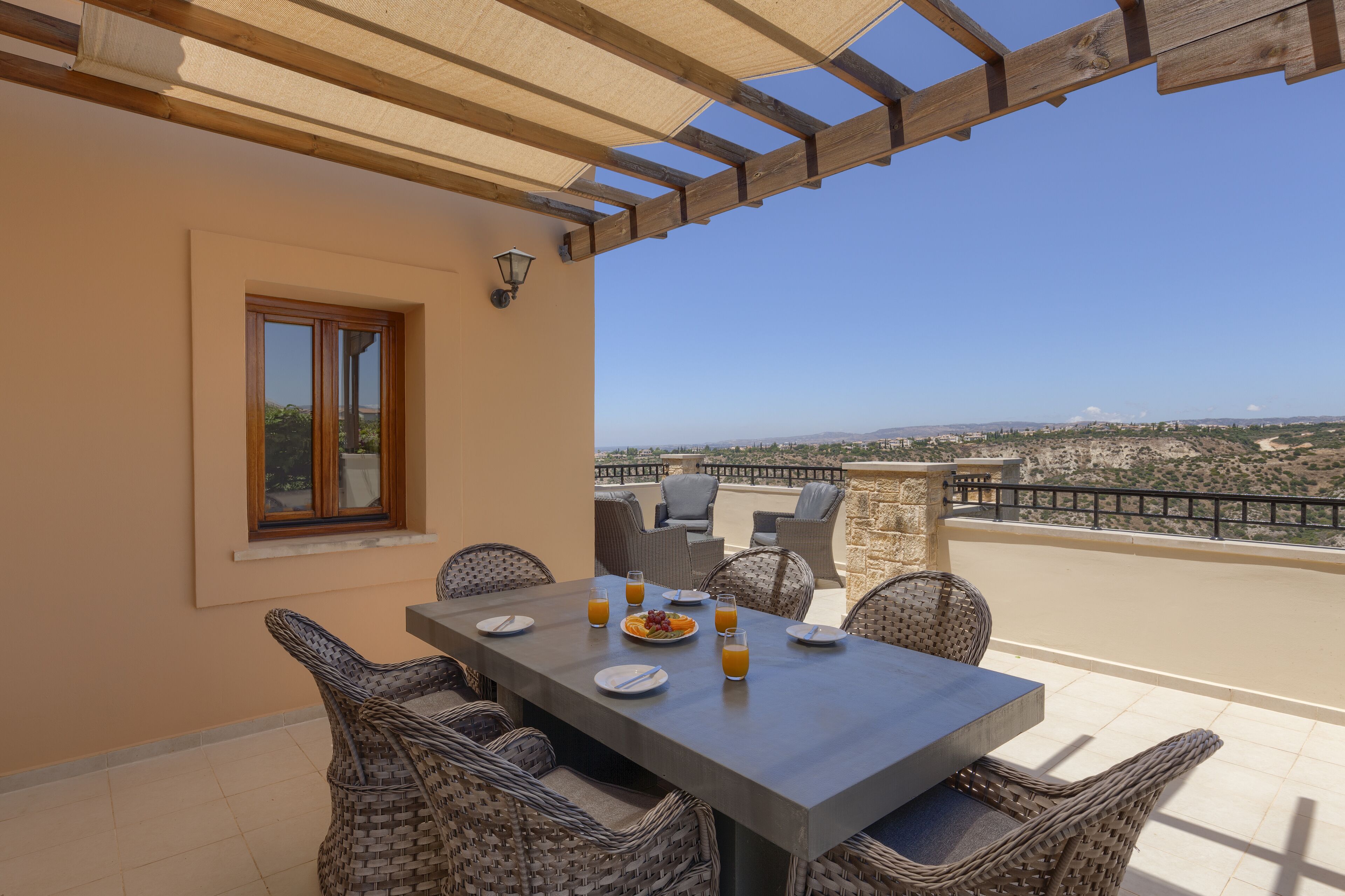 Una terraza con mesa lista para comer, sillas de mimbre y vista a la ciudad.