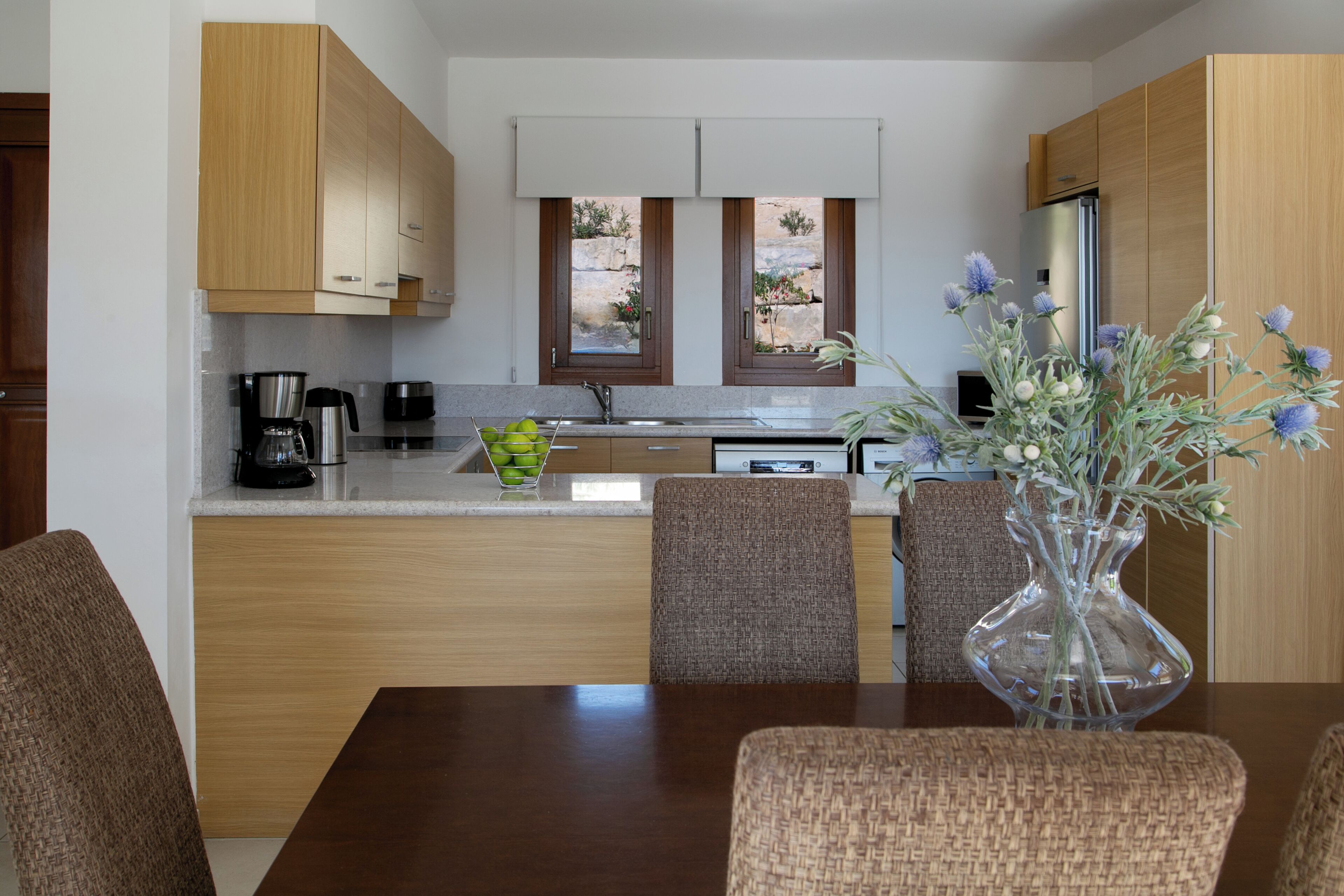A modern kitchen with wooden cabinets, a dining area with a table and chairs, and a vase with flowers on the table.