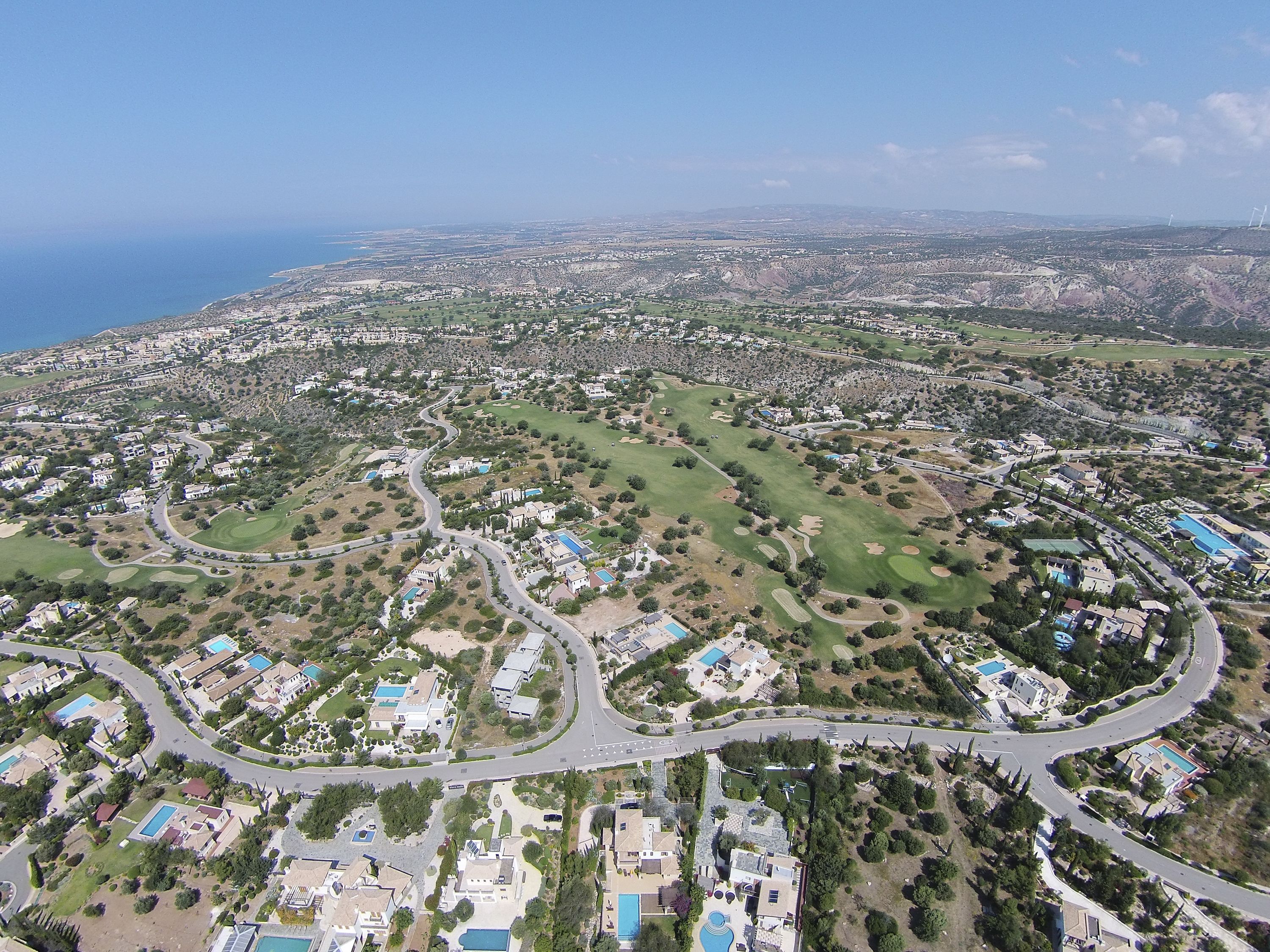 Vista aérea de una zona residencial con calles sinuosas, espacios verdes y casas con piscinas.