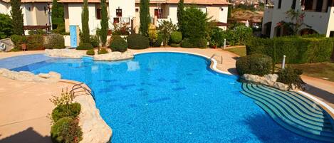 A swimming pool with a curved edge, surrounded by a landscaped garden with neatly trimmed bushes and a few tall trees.