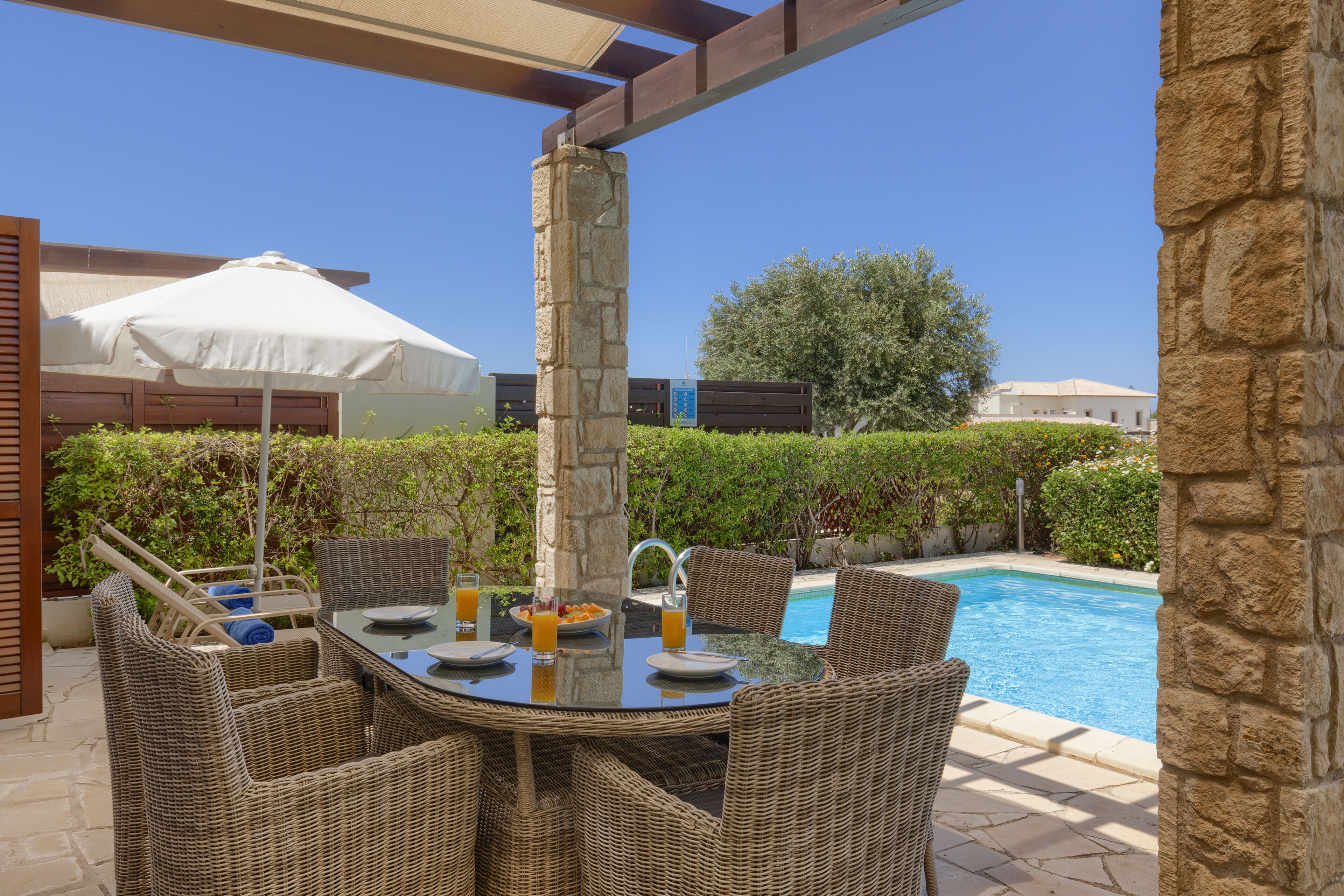 An outdoor dining area with wicker furniture, a pool, and a stone pillar.
