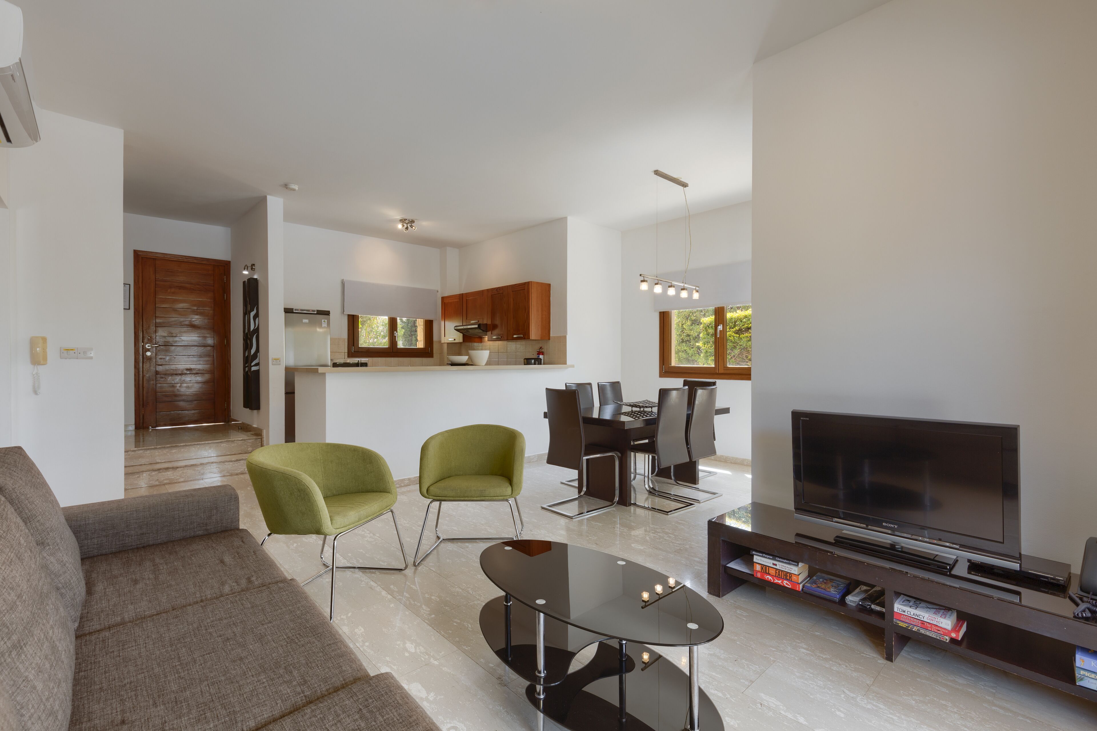 Una sala de estar moderna con un sofá, sillas, un televisor y un comedor con una mesa y sillas.