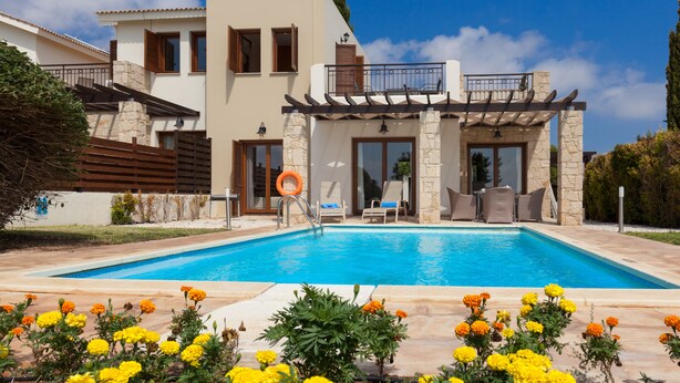 A modern house with a swimming pool, stone pillars, and a balcony with outdoor furniture. - Aphrodite Hills Rentals – Junior Villas (Kouklia)