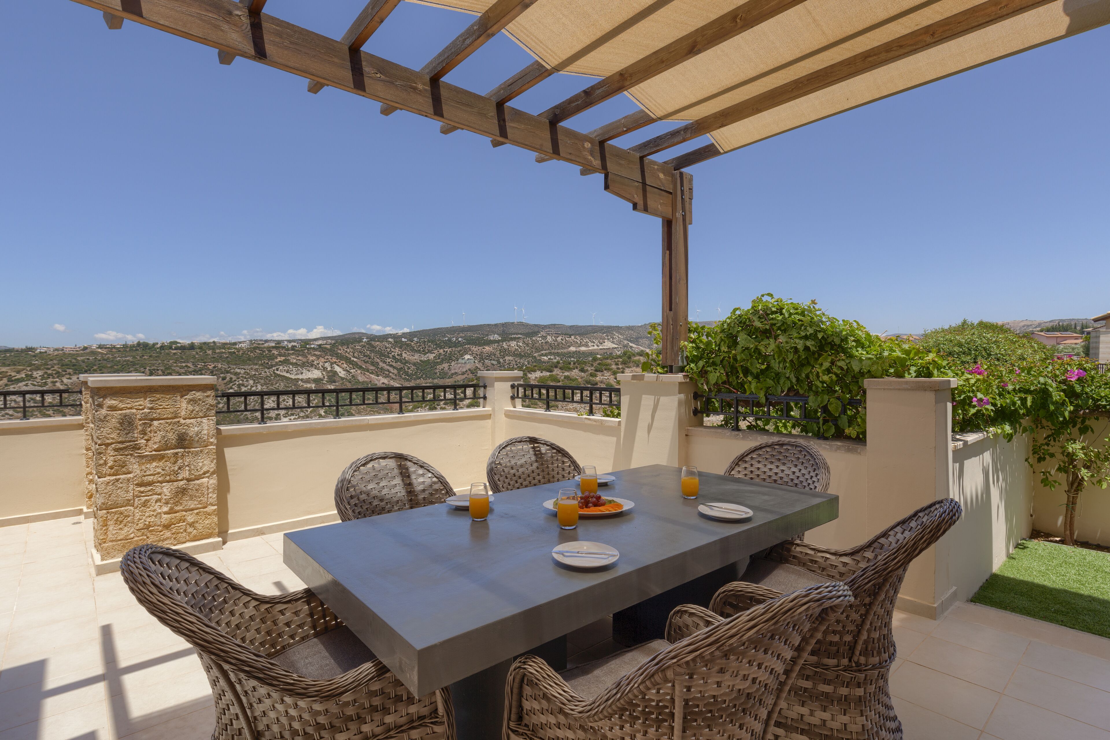 A terrace with a table set for four, overlooking a scenic landscape with hills and wind turbines.