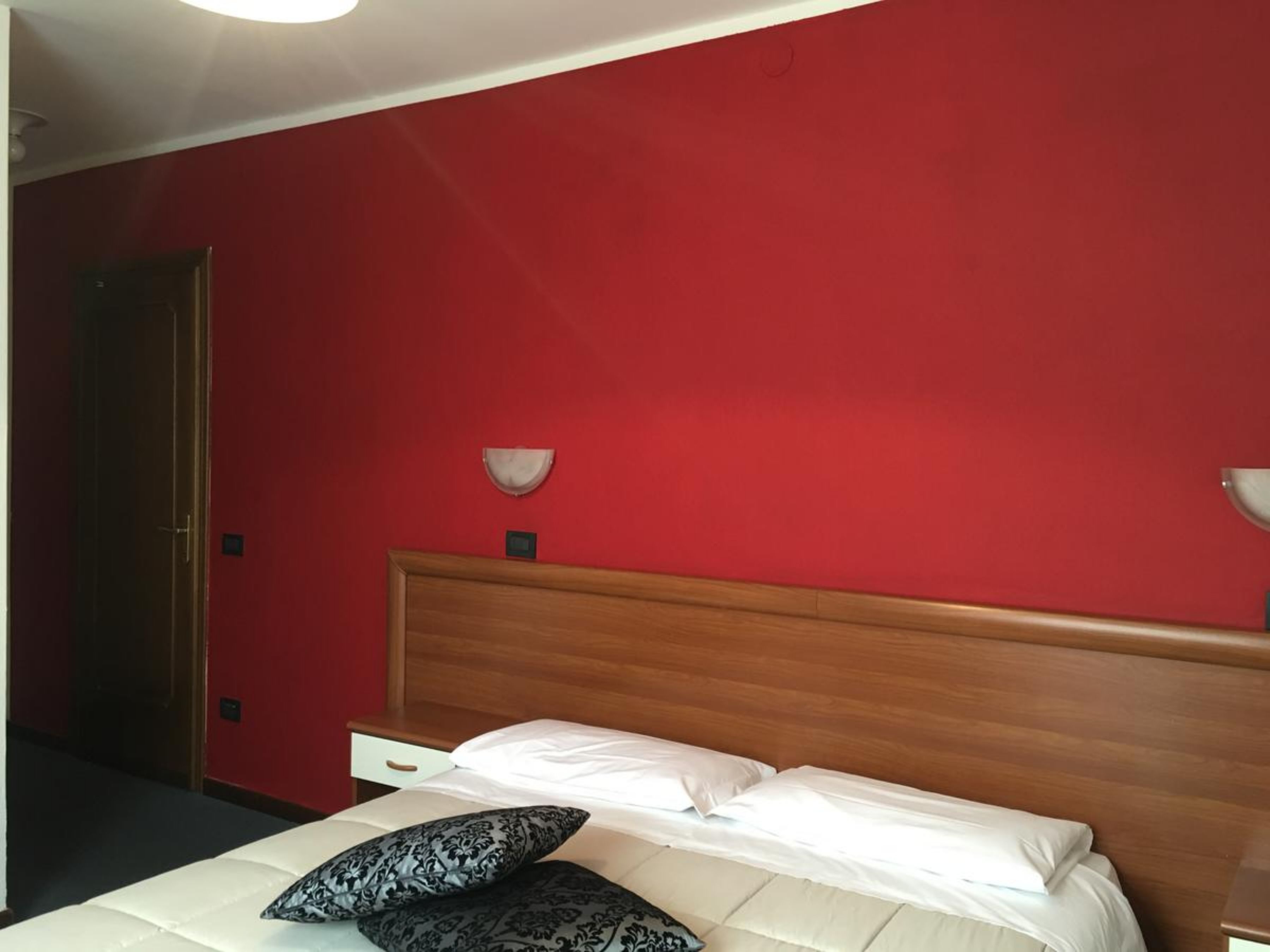 Ein Hotelzimmer mit roter Wand, einem hölzernen Kopfteil, einem Bett mit weißen Leinen und zwei Nachttischlampen.