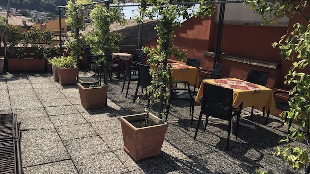 An outdoor patio with tables and chairs, surrounded by potted plants and a view of a mountainous landscape. - Hotel Cortina (Garda)