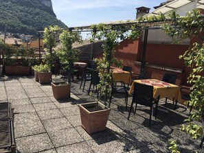 Un patio al aire libre con mesas y sillas, rodeado de plantas en macetas y vistas a un paisaje montañoso.