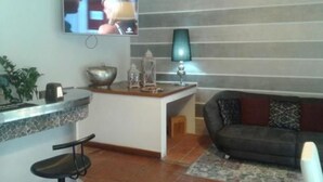 A modern living room with a sofa, a coffee table, and a TV mounted on the wall. - Hotel Cortina (Garda)